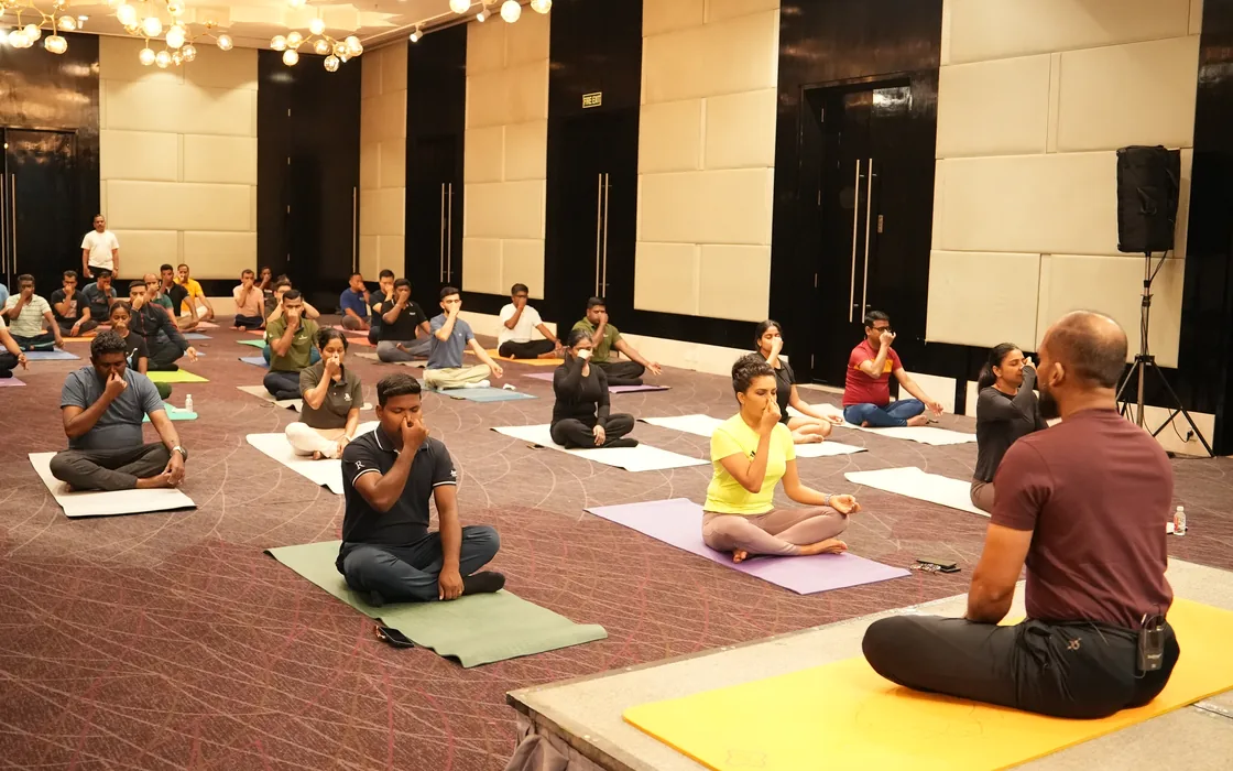 Abhilash seated facing a hotel ballroom of participants in meditation at the Renaissance, Bengaluru.